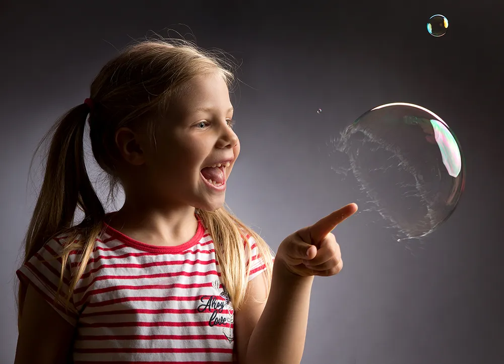 Kindershooting: Ein kleines Mädchen lässt eine Seifenblase platzen – Kinderfotografie im Fotostudio Foto Ape in Rostock