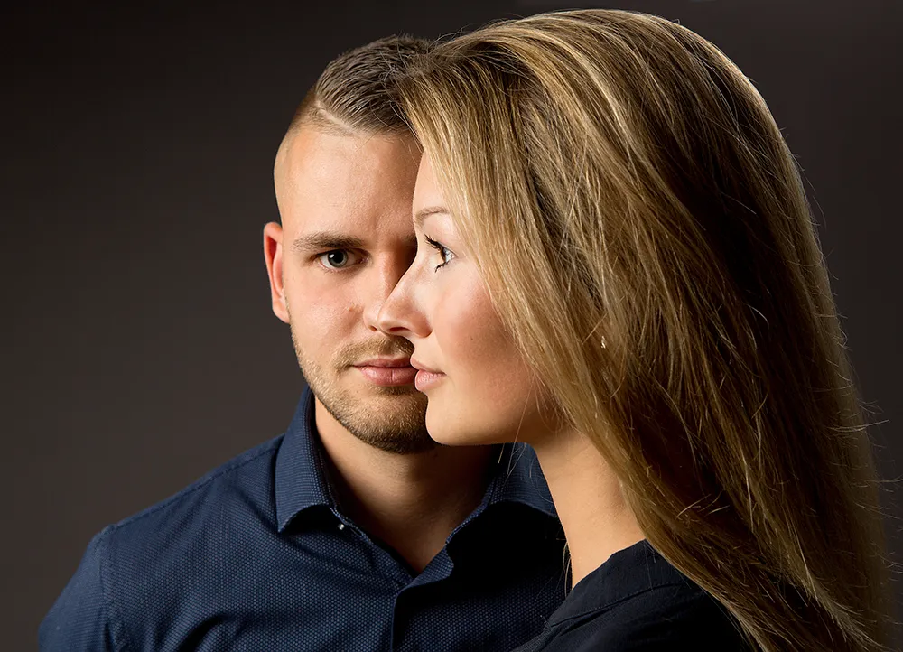 Portraitfoto eines Paares – Frau steht seitlich vor dem Mann vor dunklem Hintergrund im Fotostudio Foto Ape in Rostock